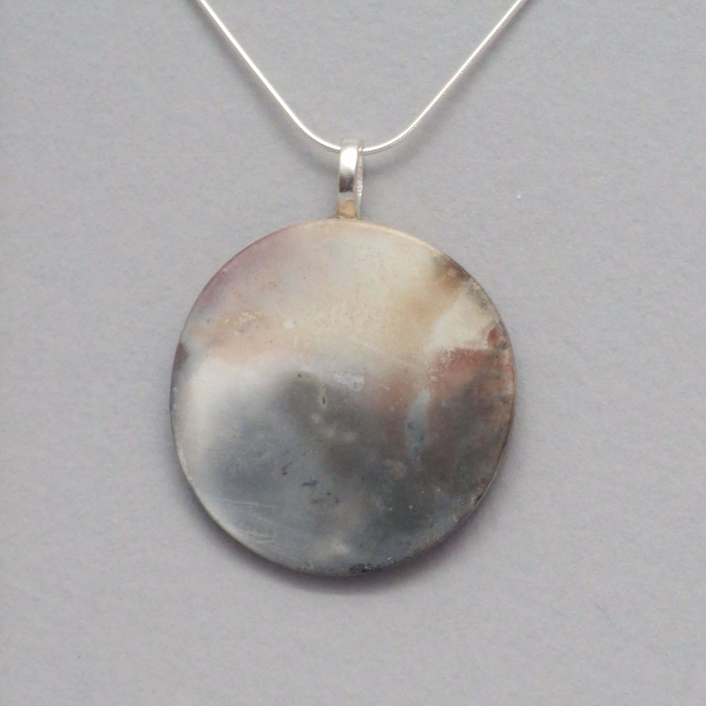 Smoke fired ceramic pendant with an etherial pattern on black necklace