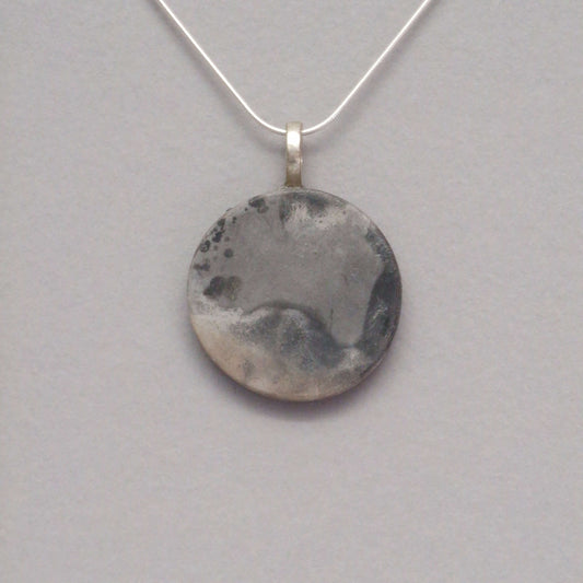 smoke fired ceramic pendant in soft grey colours on a black necklace