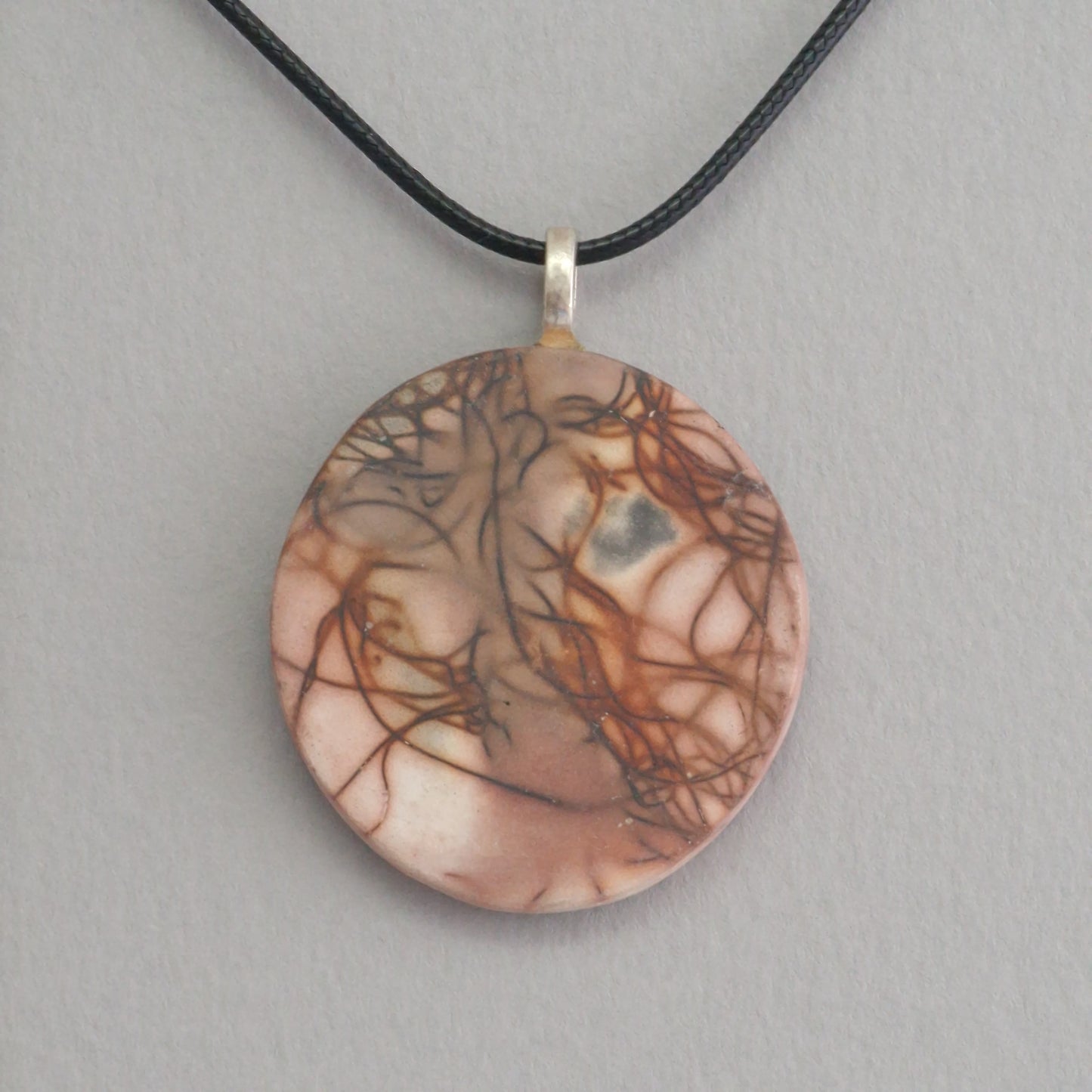 Unique smoke fired ceramic pendant with orange line pattern on a black necklace
