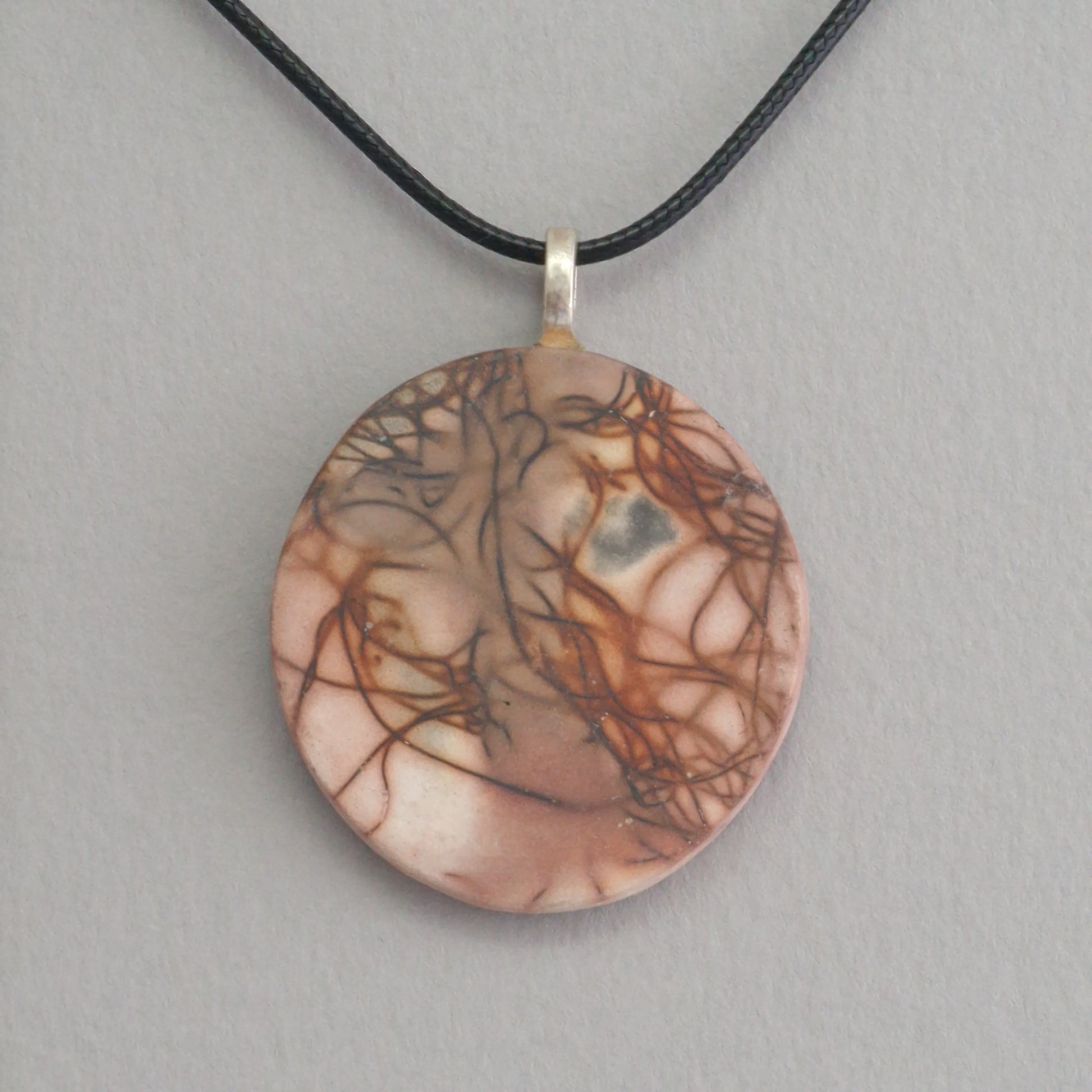 Unique smoke fired ceramic pendant with orange line pattern on a black necklace