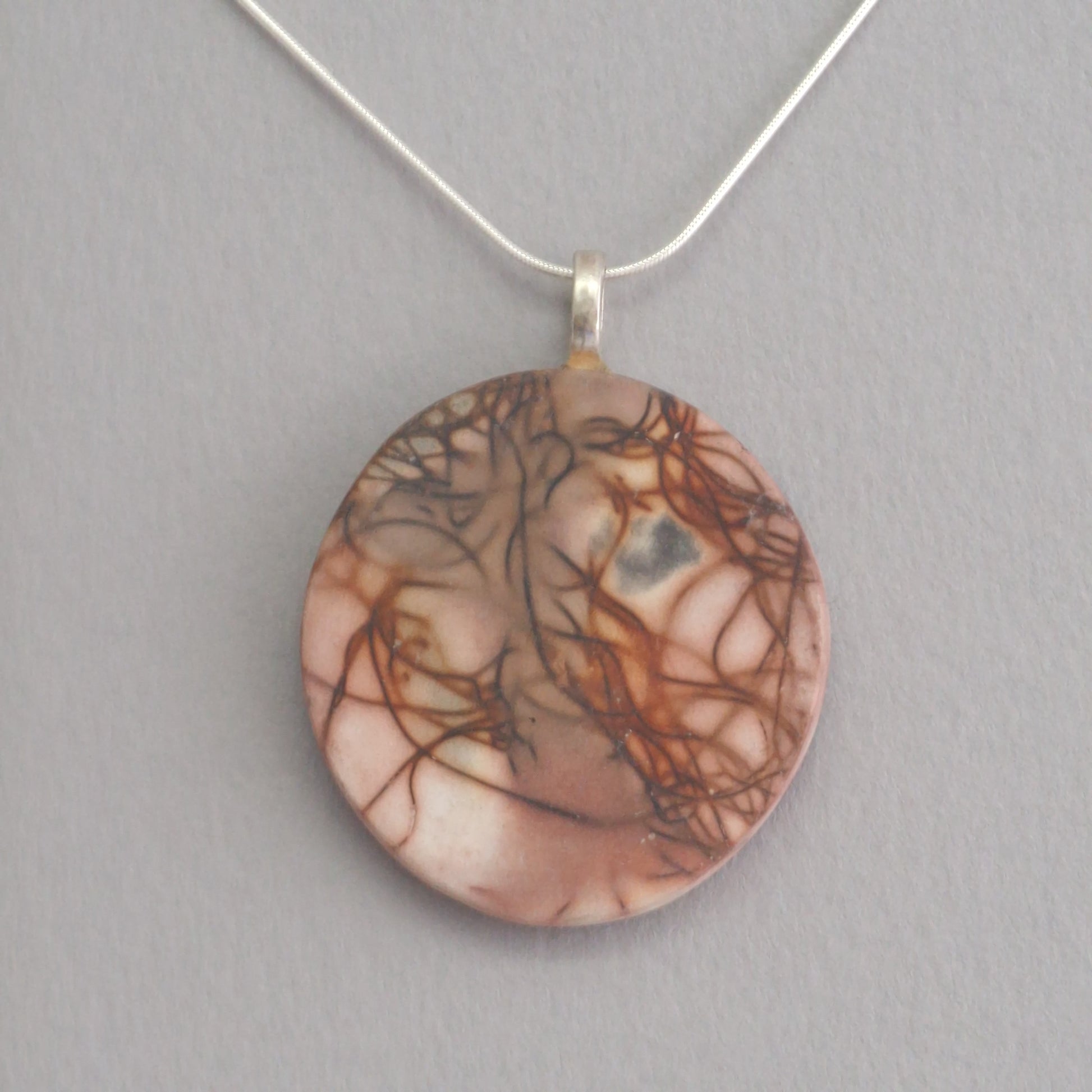 Unique smoke fired ceramic pendant with orange line pattern on a black necklace