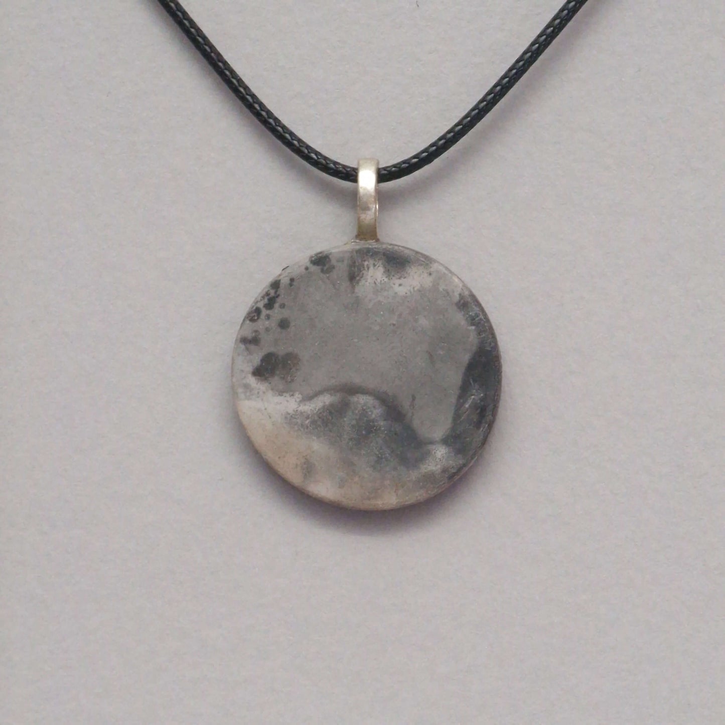 smoke fired ceramic pendant in soft grey colours on a black necklace